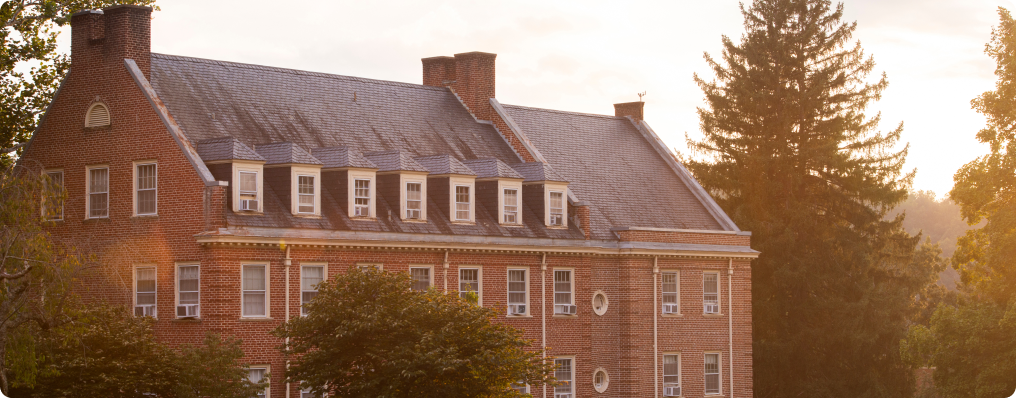 A large, three-story brick building with multiple dormer windows and chimneys, surrounded by trees in the early evening sunlight, stands as a symbol of SVU’s rich history and welcoming atmosphere for new students navigating college admissions.