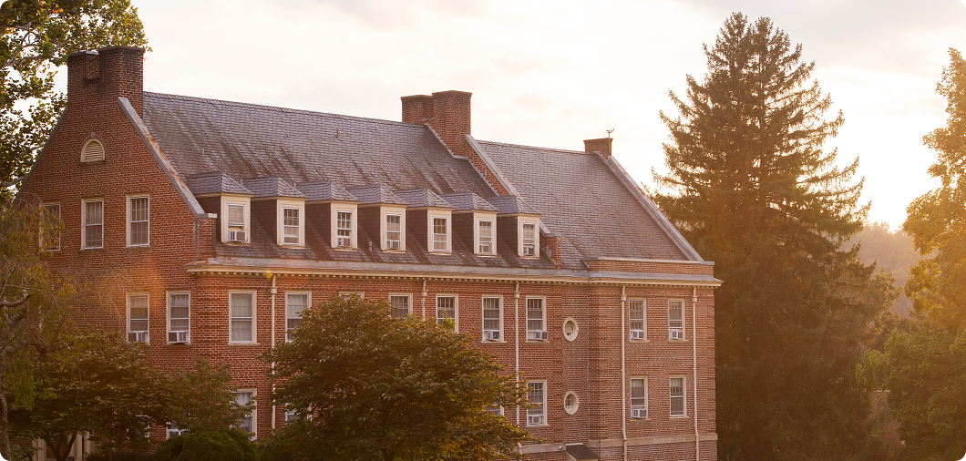 SVU Campus; A large brick building with multiple windows and a sloped roof, surrounded by trees, pictured at sunset.