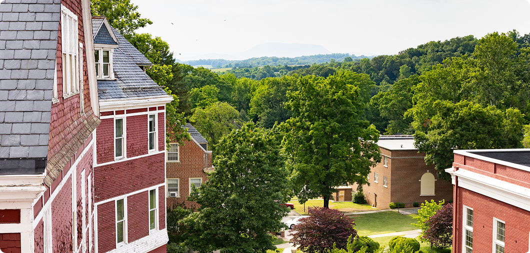Red brick buildings with white trim are surrounded by green trees on the SVU campus, with hills and a distant mountain visible under a bright sky.