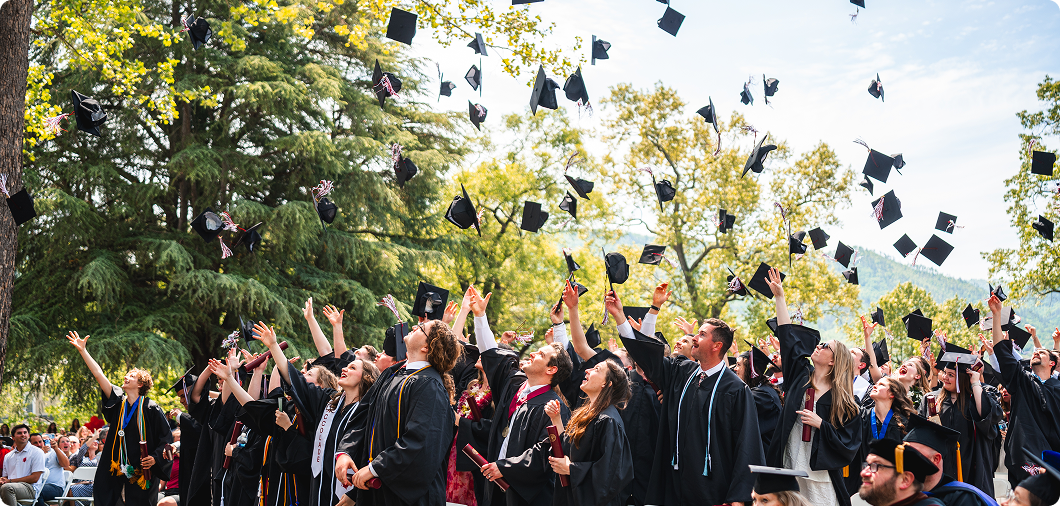 A large group of graduates in caps and gowns, some reflecting on their SVU journey and financial aid support, toss their caps into the air during an outdoor graduation ceremony.